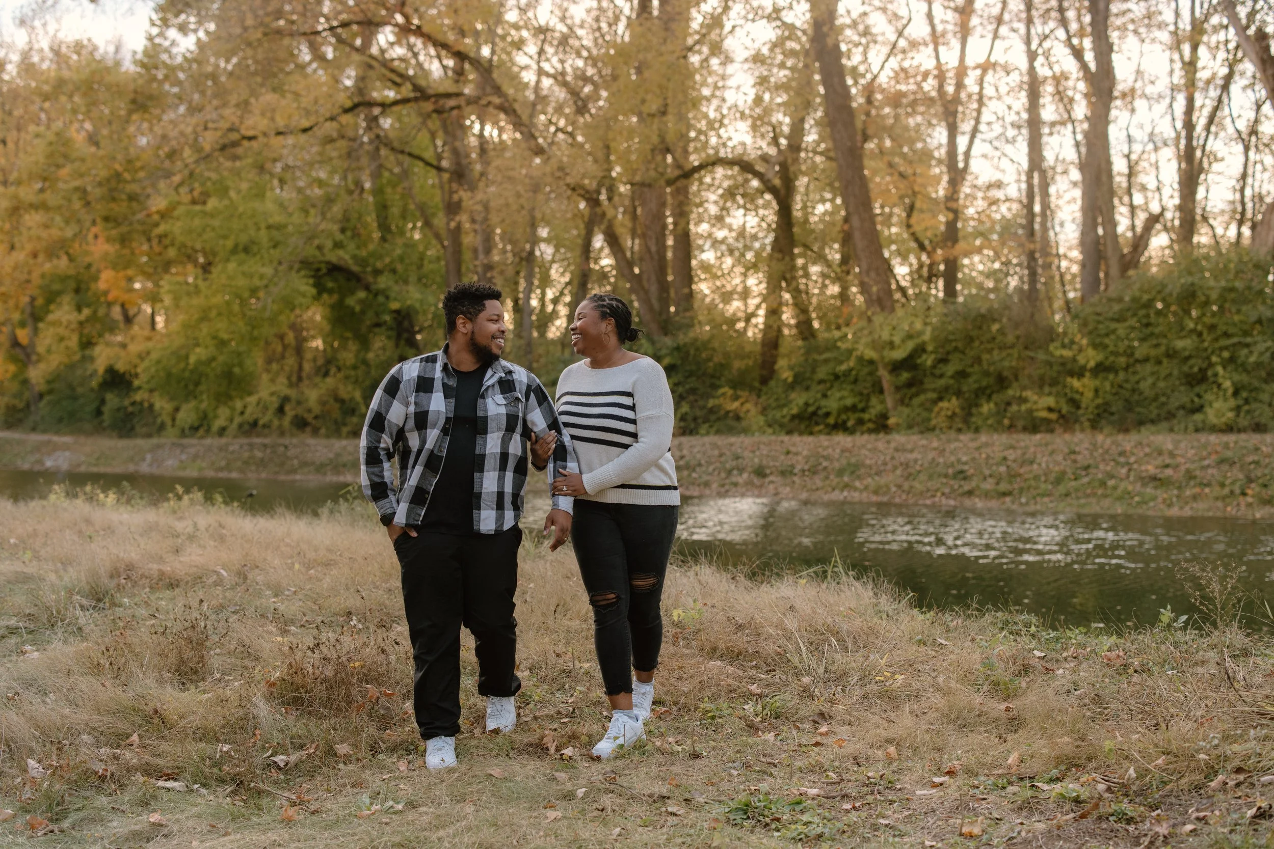 A smiling family of three sitting on a picnic blanket in a park during autumn, with trees and fallen leaves in the background.