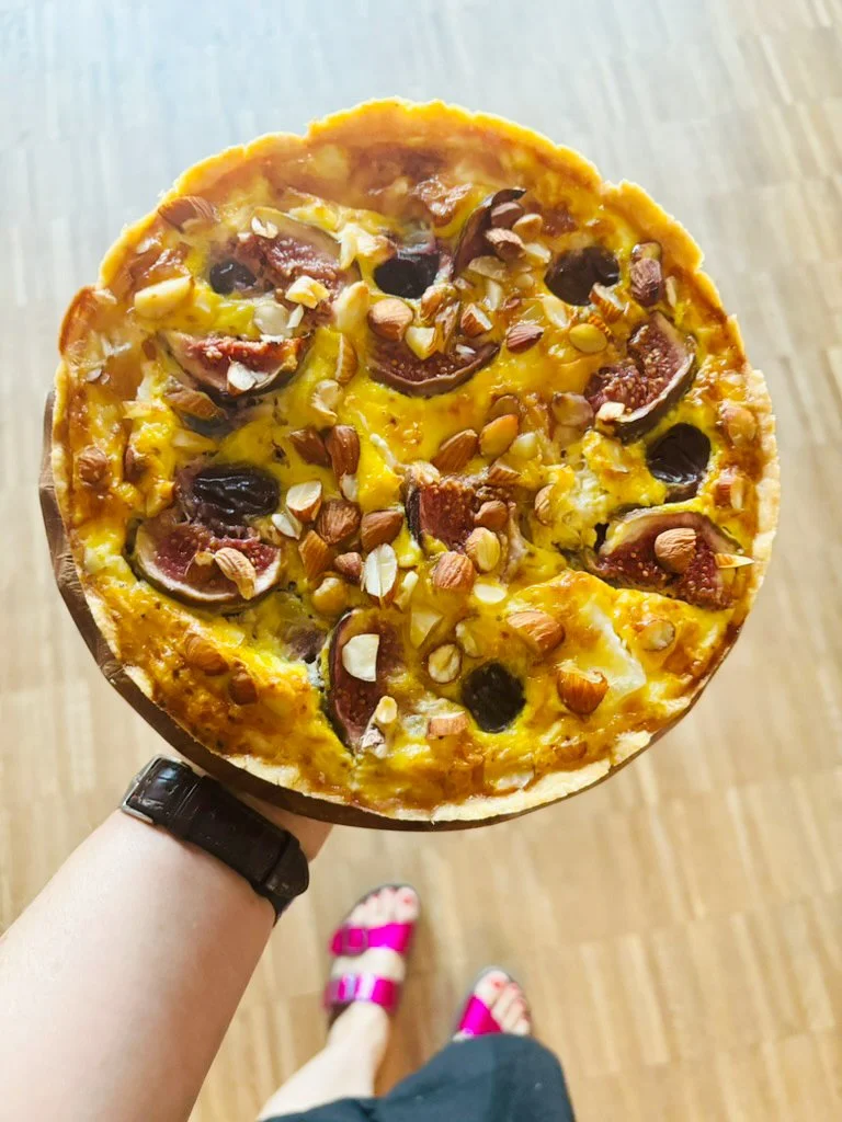 Eine Pizza mit Belag aus dunklen Oliven, gehackten Nüssen, Käse und Fleisch auf einem runden Pizzaboden.