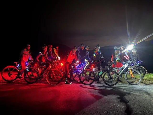 Bike Lane Gravel riders with helmets with Christmas lights, riding bikes at night outdoors.