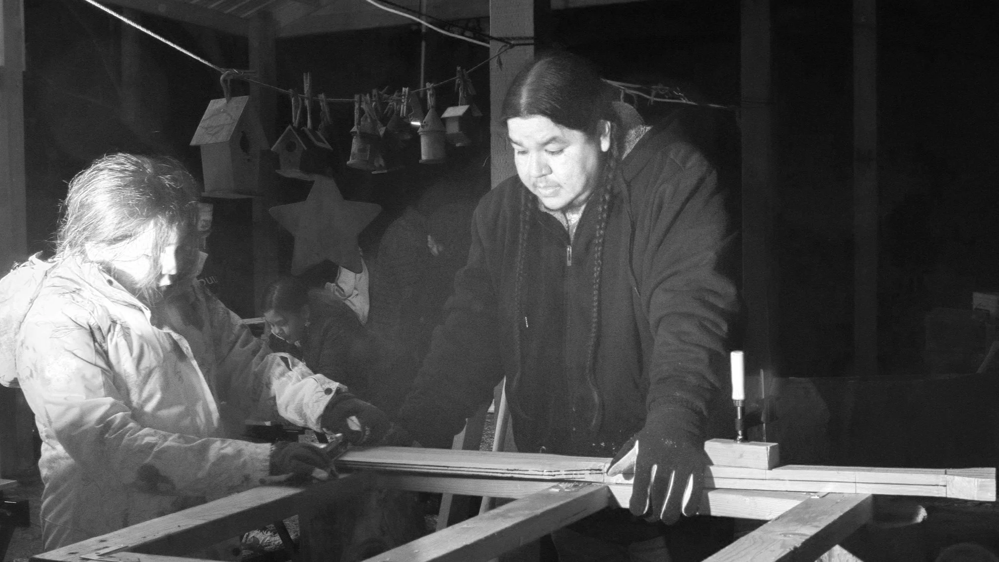 A group of people working together at a table, with birdhouses hanging in the background.