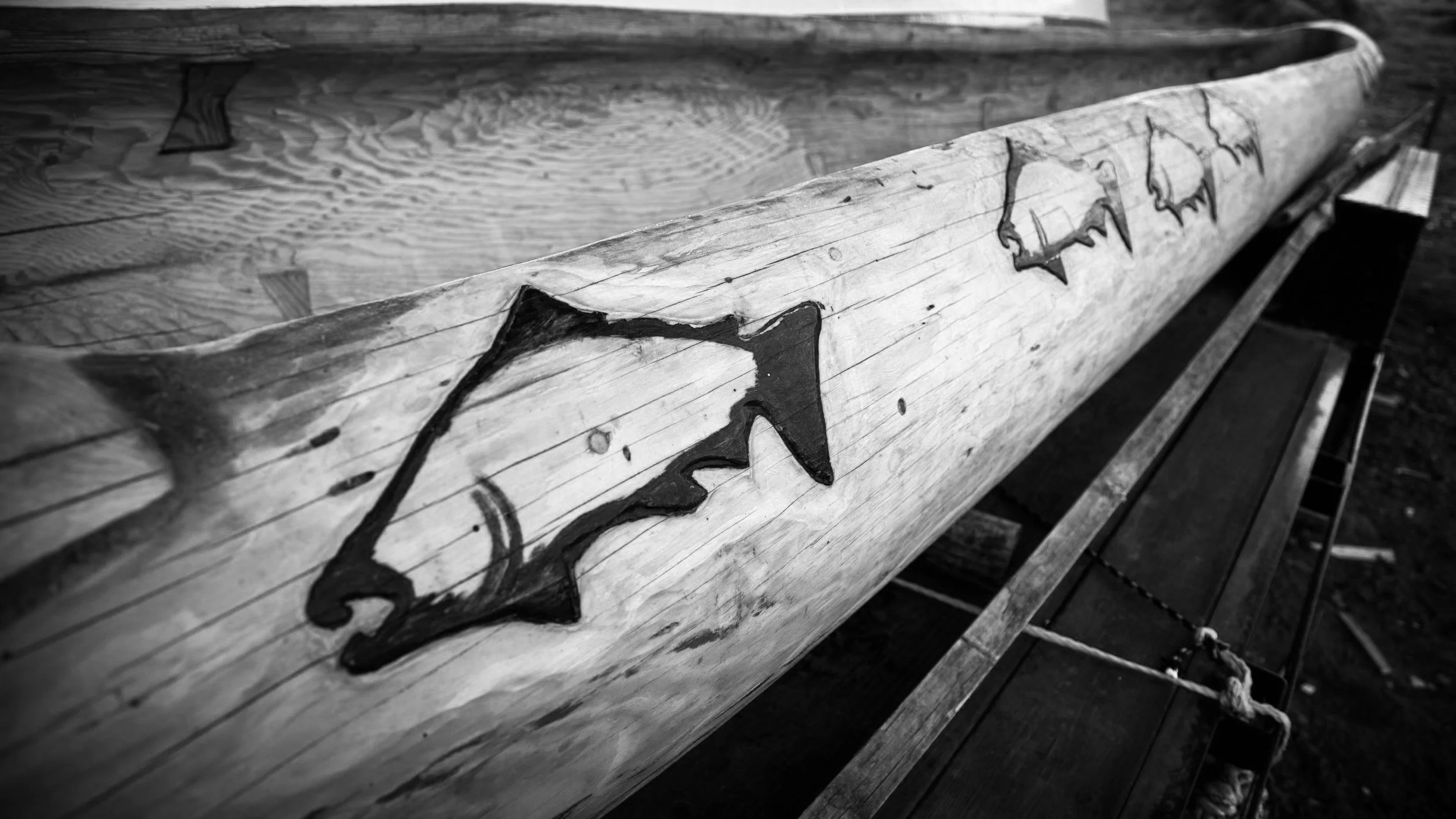 A black and white photo of a wooden bench with graffiti on it, situated outdoors.