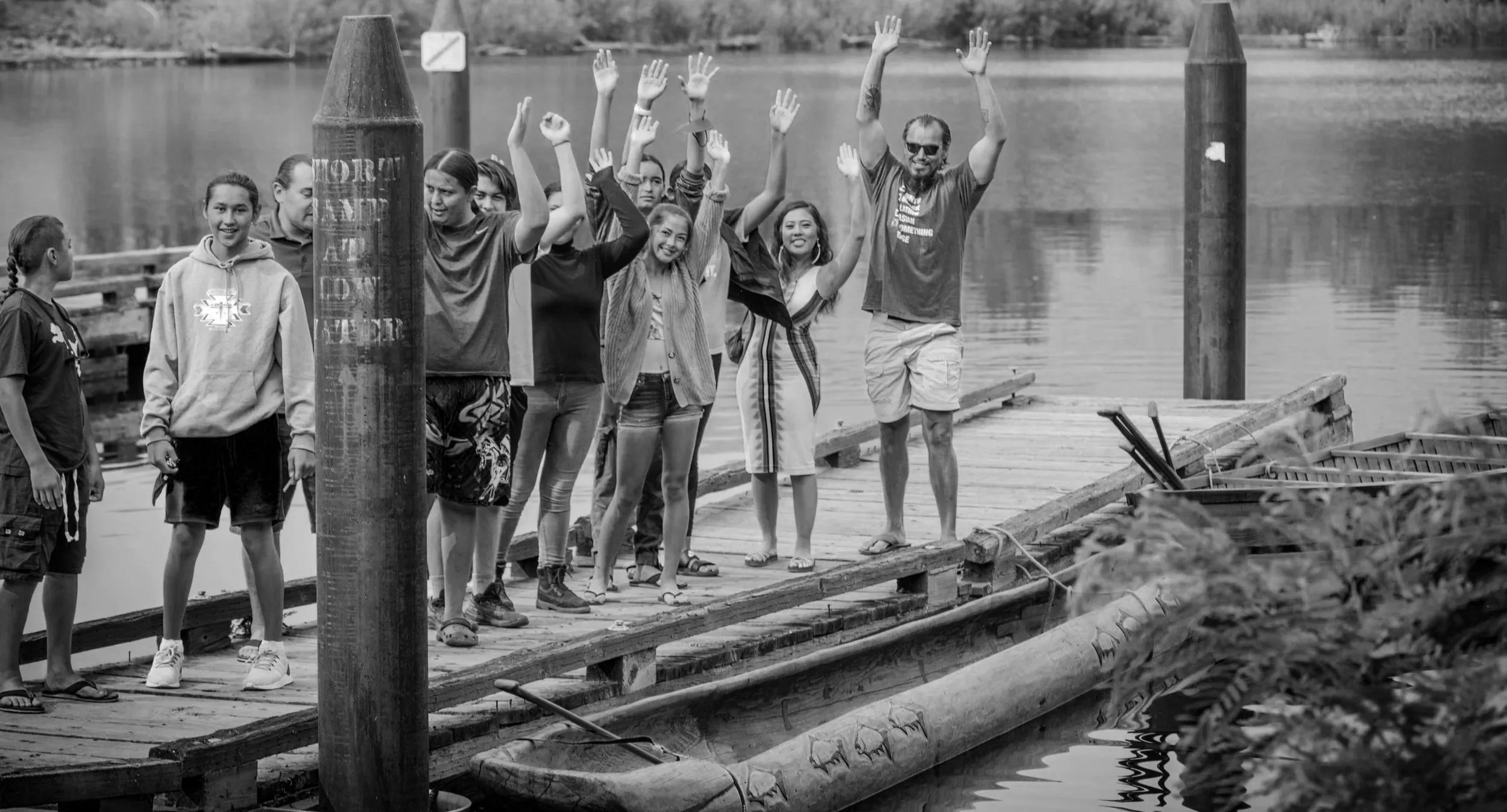 A group of people, including children and an adult man, standing on a wooden dock near a body of water, waving and smiling.