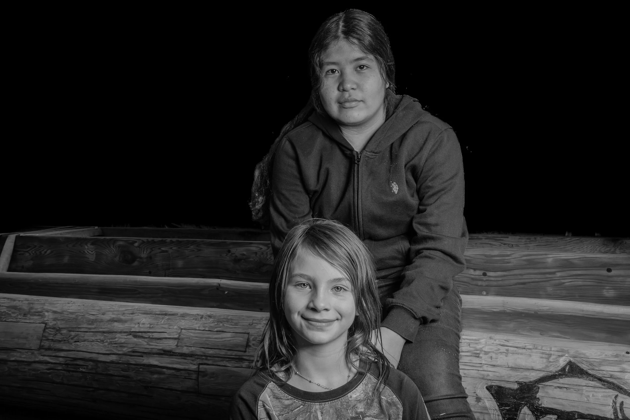 Black and white photo of two young girls, one with long hair and the other with shorter hair, posing in front of a dark background.