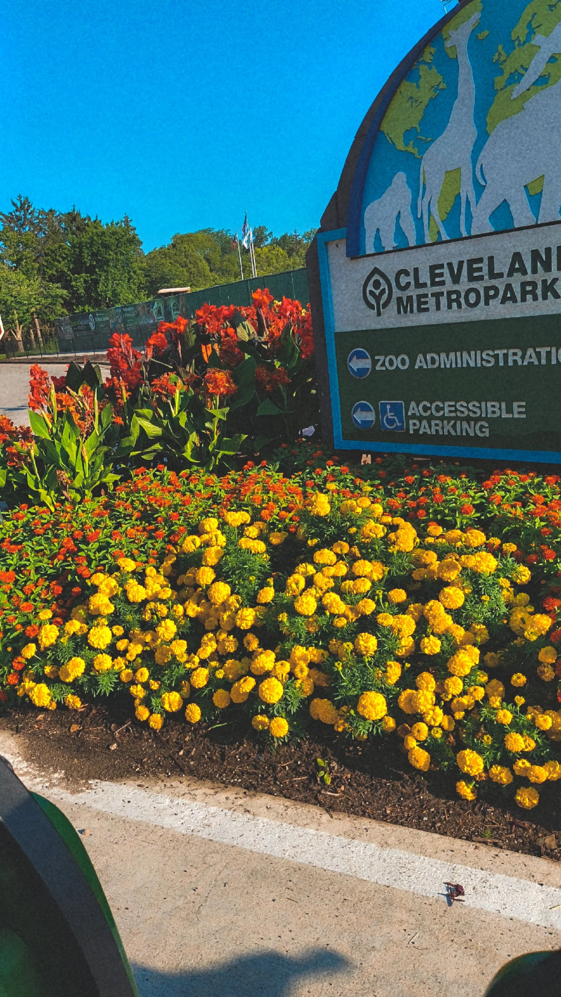 Sign at Cleveland Metroparks zoo with flower beds of yellow and orange flowers in the foreground and blue sky in the background.