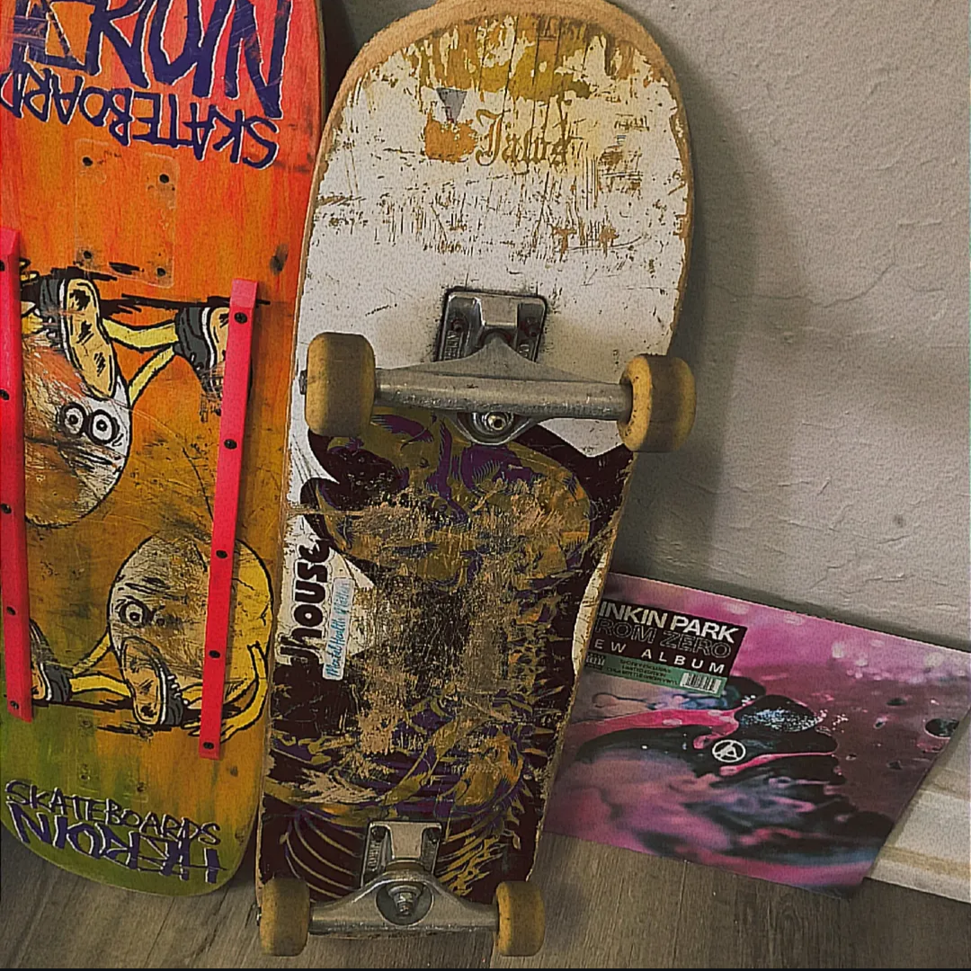 Two skateboards leaning against a wall with a pink vinyl record album cover on the floor beside them.