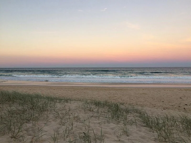 Scenic view of the beach at sunset with waves, sandy shore, and grass in the foreground