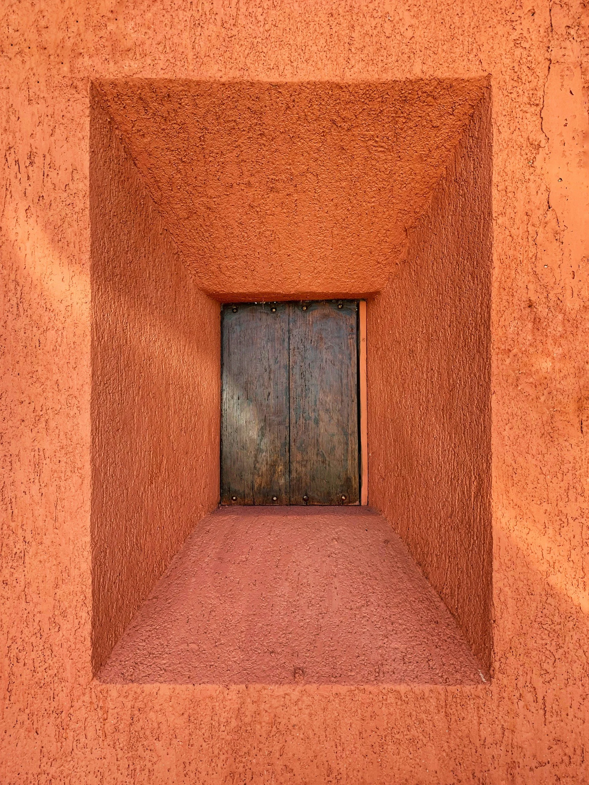 Close-up of a wooden door set into a textured orange stucco wall with a recessed rectangular frame.
