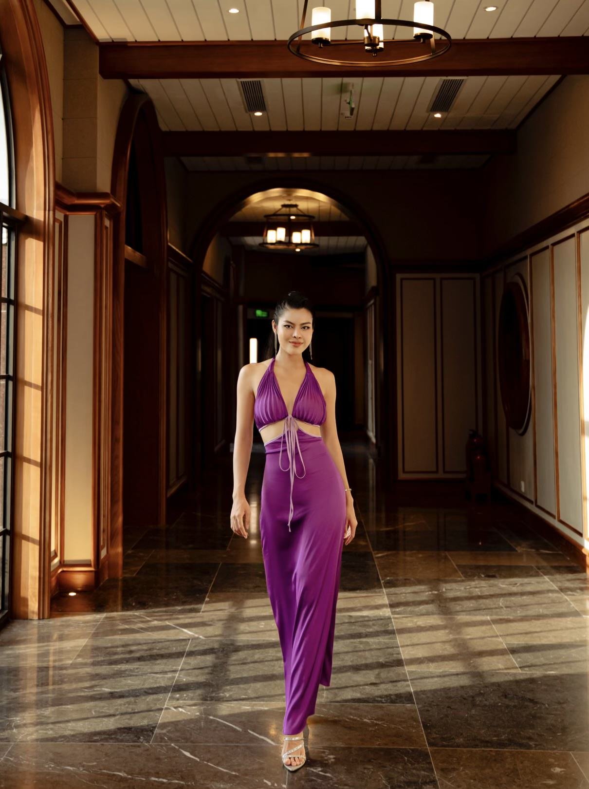 A woman in a purple halter dress walking in a hotel hallway with wooden paneling and lamps.
