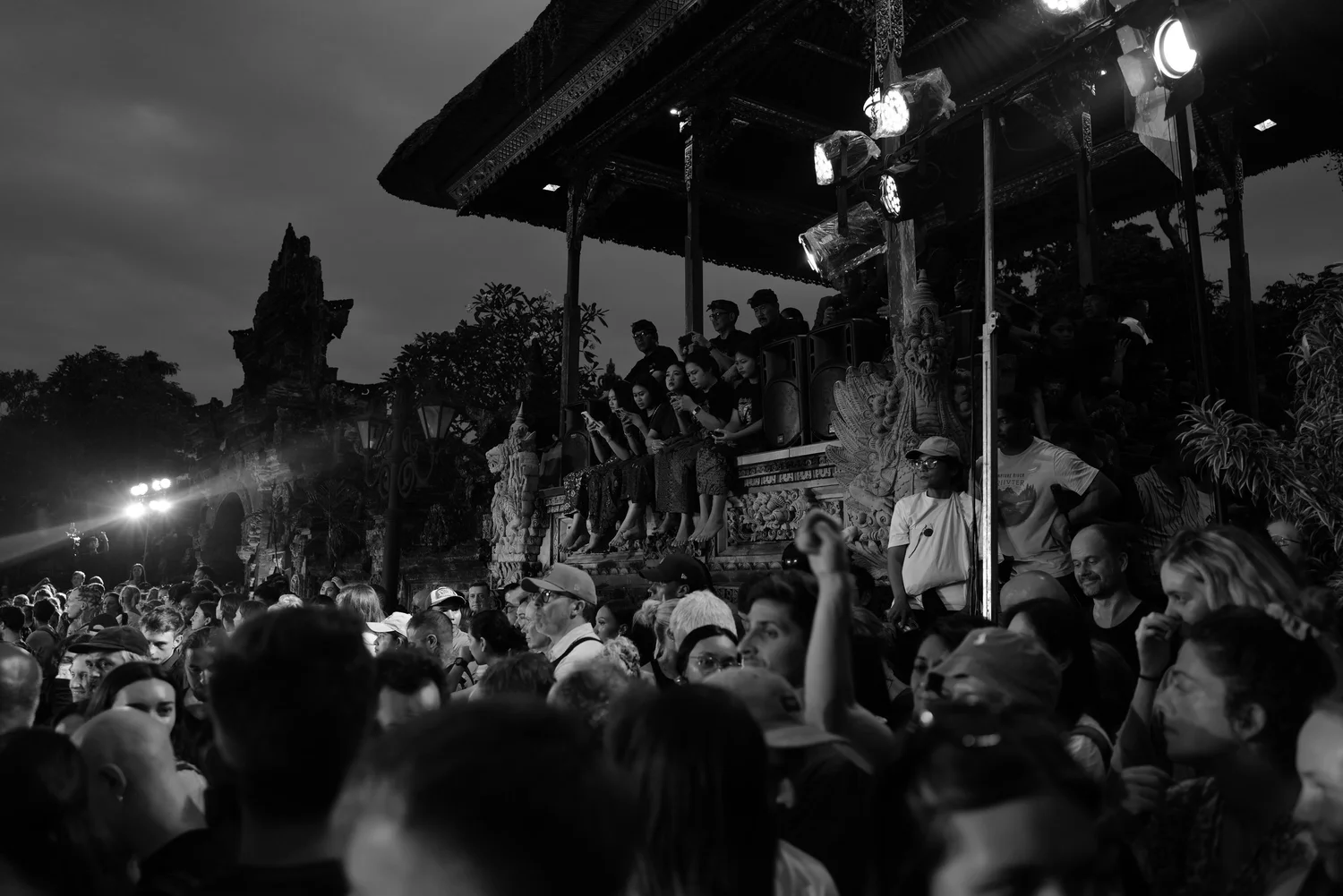 The crowd gathers beneath lights as evening falls