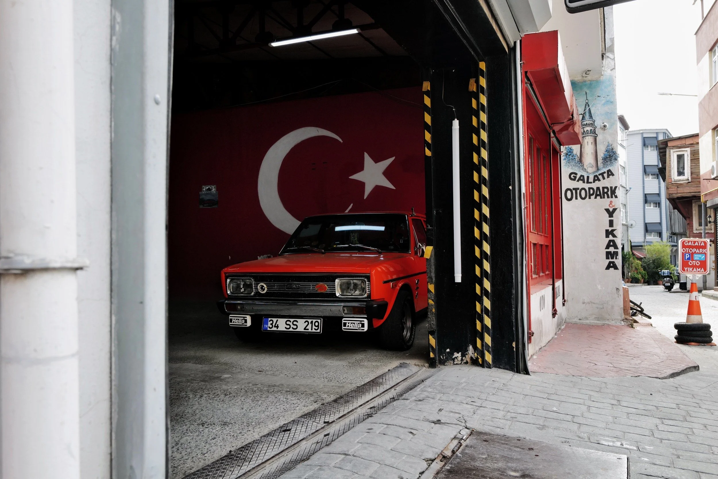 A red car parked beneath a Turkish flag