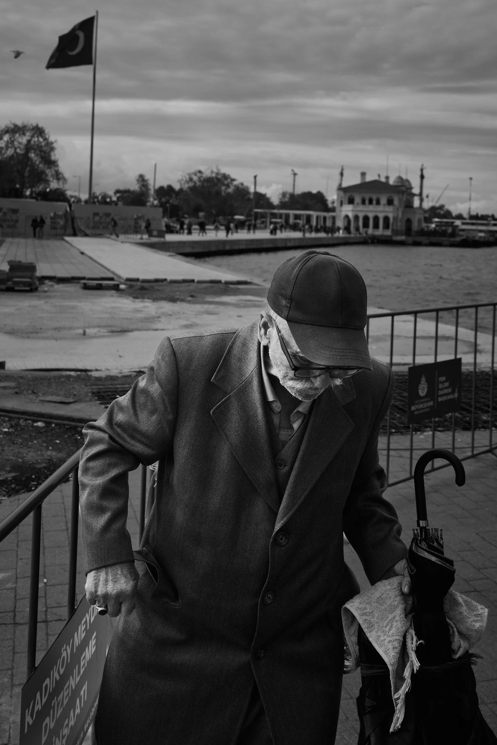 An older man with a cap and umbrella by the waterfront