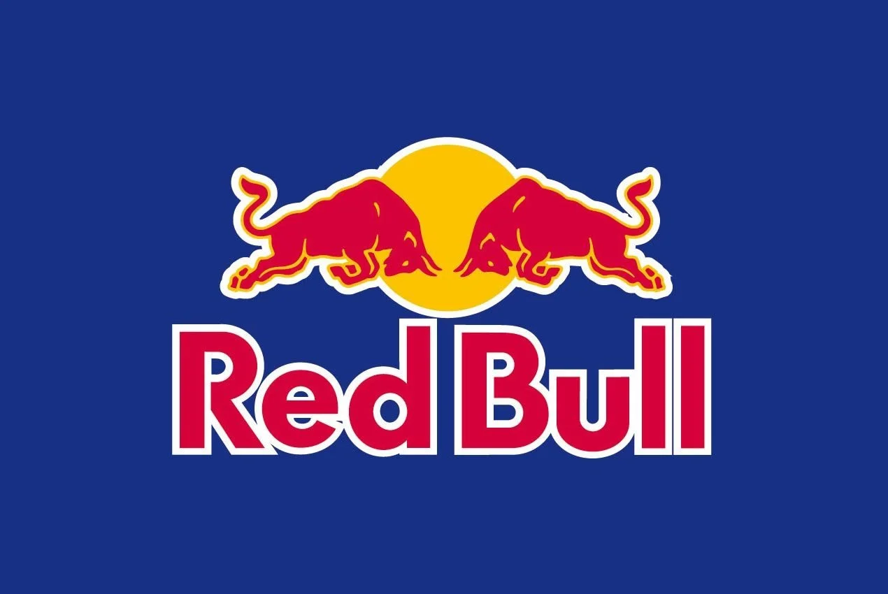 Red Bull logo with two red bulls facing each other in front of a yellow sun on a blue background.