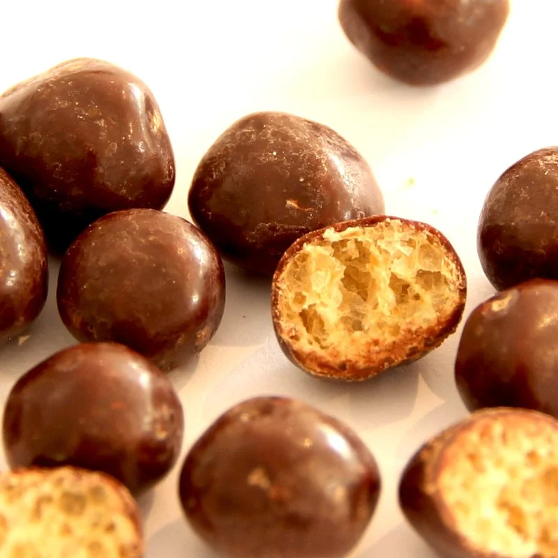 Close-up of chocolate-covered caramel candies, some cut in half to show the caramel filling.