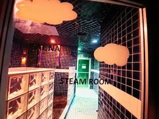 Glass entrance door to the steam room at The Works Indianapolis with tiled walls and illuminated interior lighting.