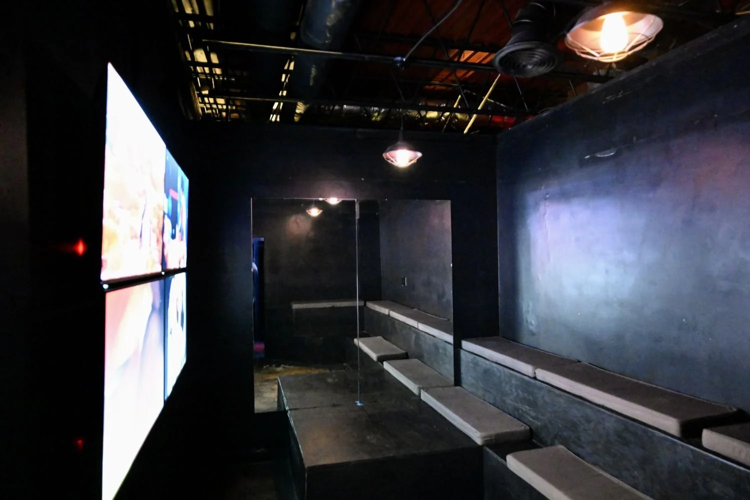 Second-floor group video room at The Works Indianapolis with tiered seating, large screens, and dark lounge lighting.