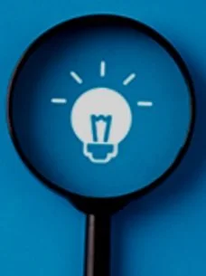 Magnifying glass focusing on a light bulb icon, symbolizing ideas or discovery, on a blue background.
