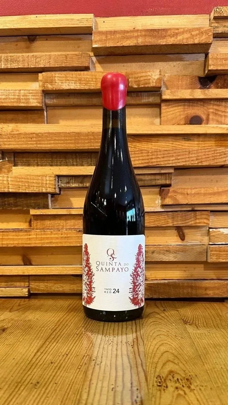 A bottle of Quinta do Sampeiro Colheita 2023 wine on a wooden surface with a wooden wall background.