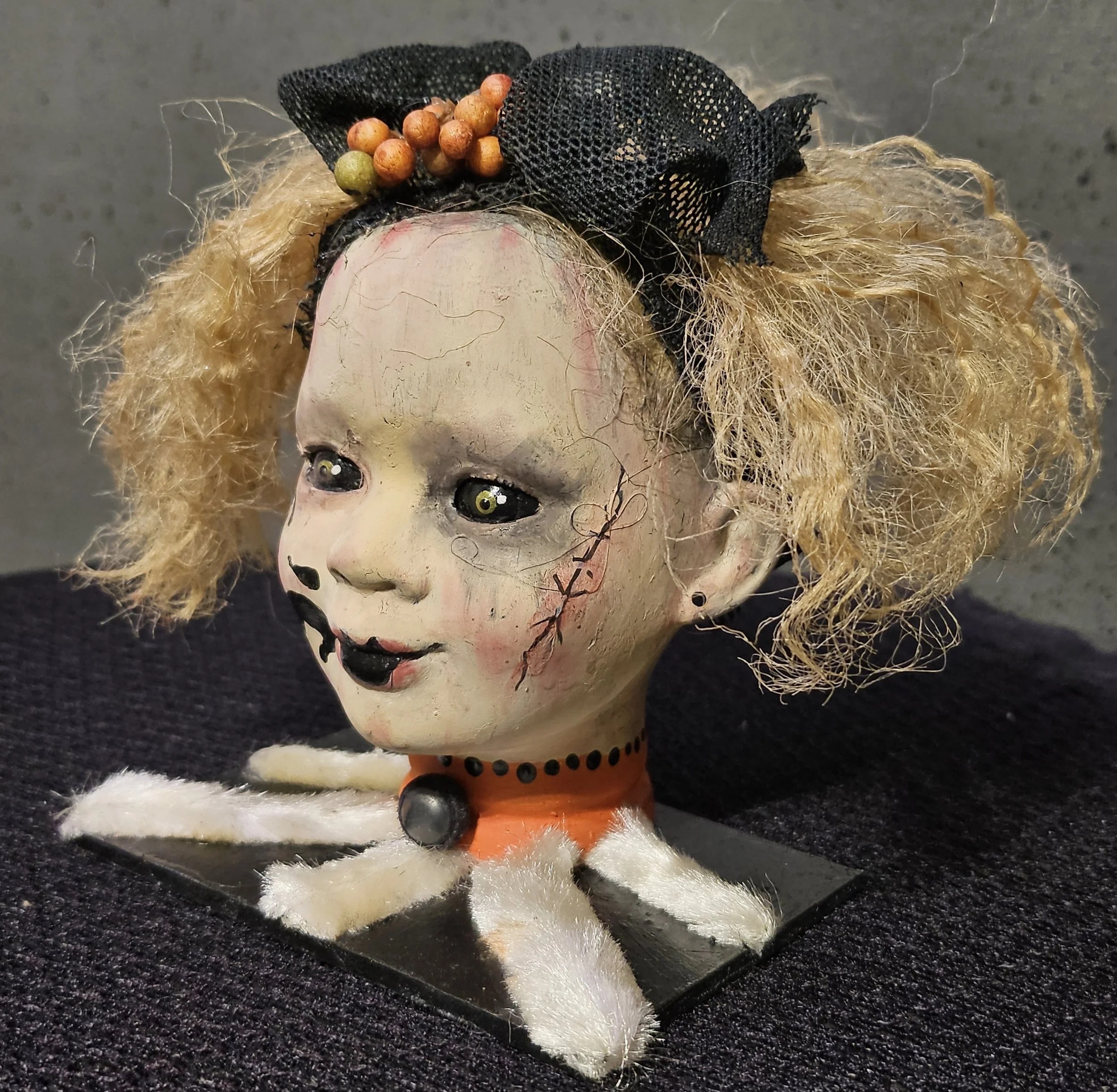  Left-side view of Ida, a handmade recycled horror doll with blonde curls, cracked skin, stitched scars, black lips, and a large black bow. 