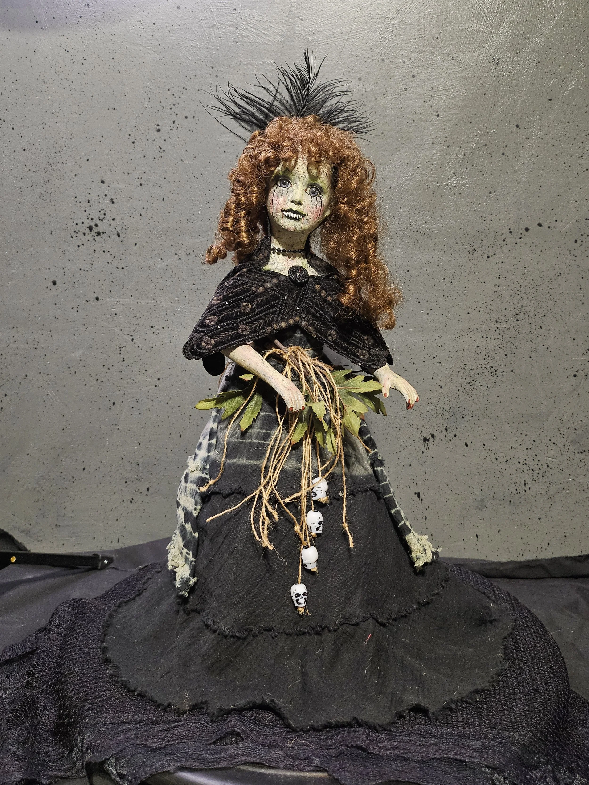  Lady Nightshade, a handmade gothic doll with curly auburn hair, a black feather headpiece, velvet cape, leafy skull belt, and flowing black dress. 