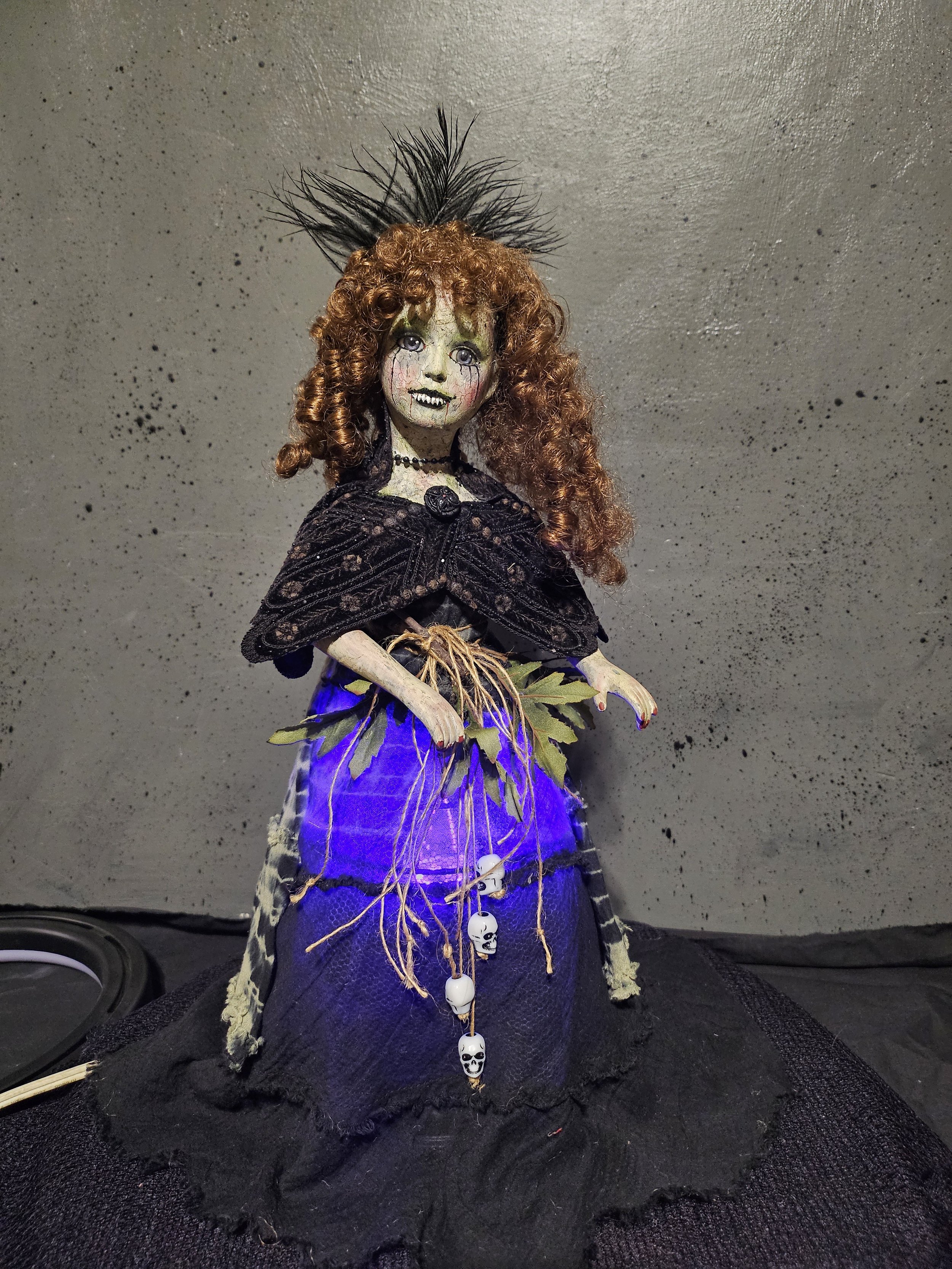  Lady Nightshade illuminated from beneath her black dress with an eerie purple glow, surrounded by leafy details, hanging roots, and miniature skulls. 