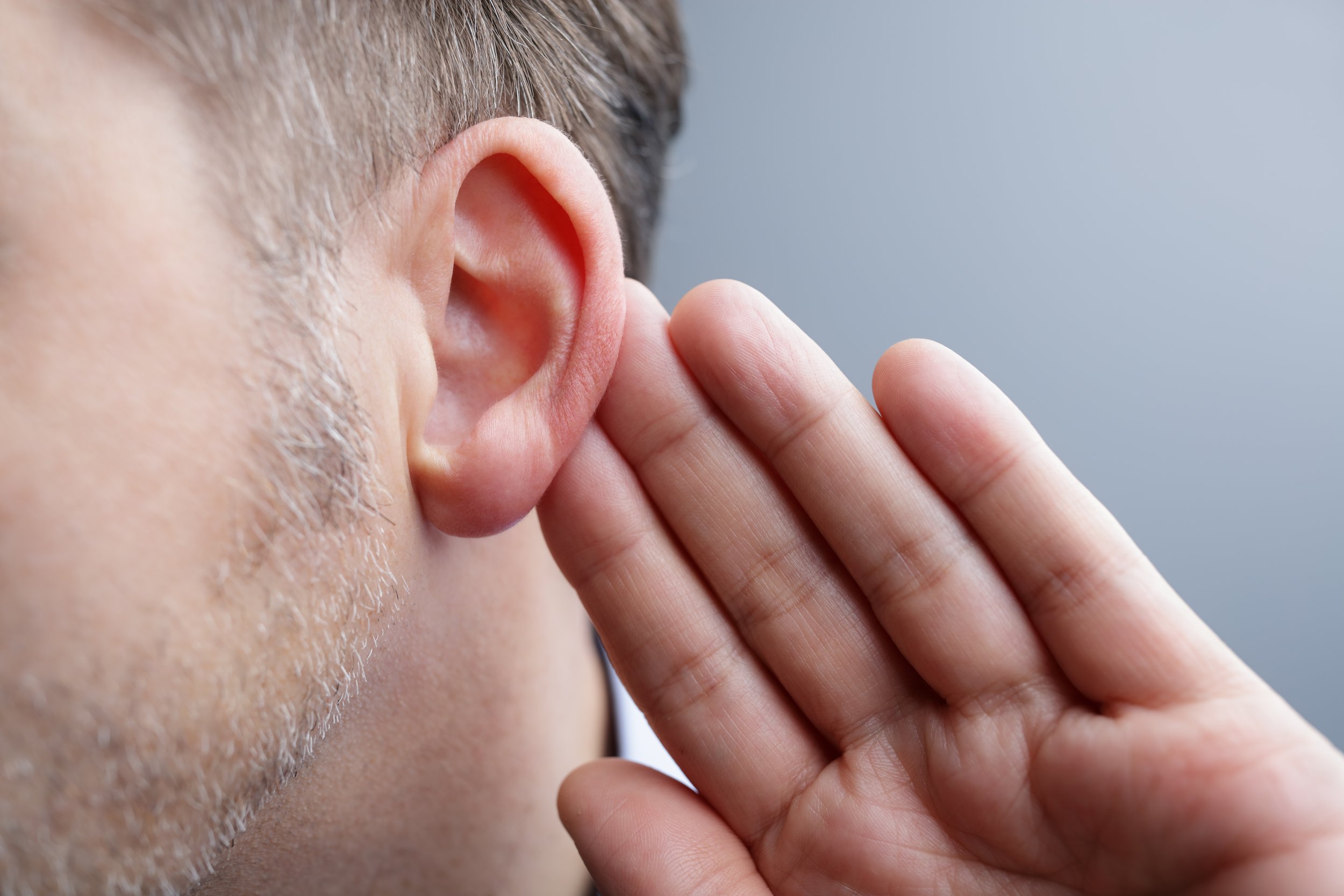 Close-up of a person with short hair and stubble whispering into their hand near their ear.