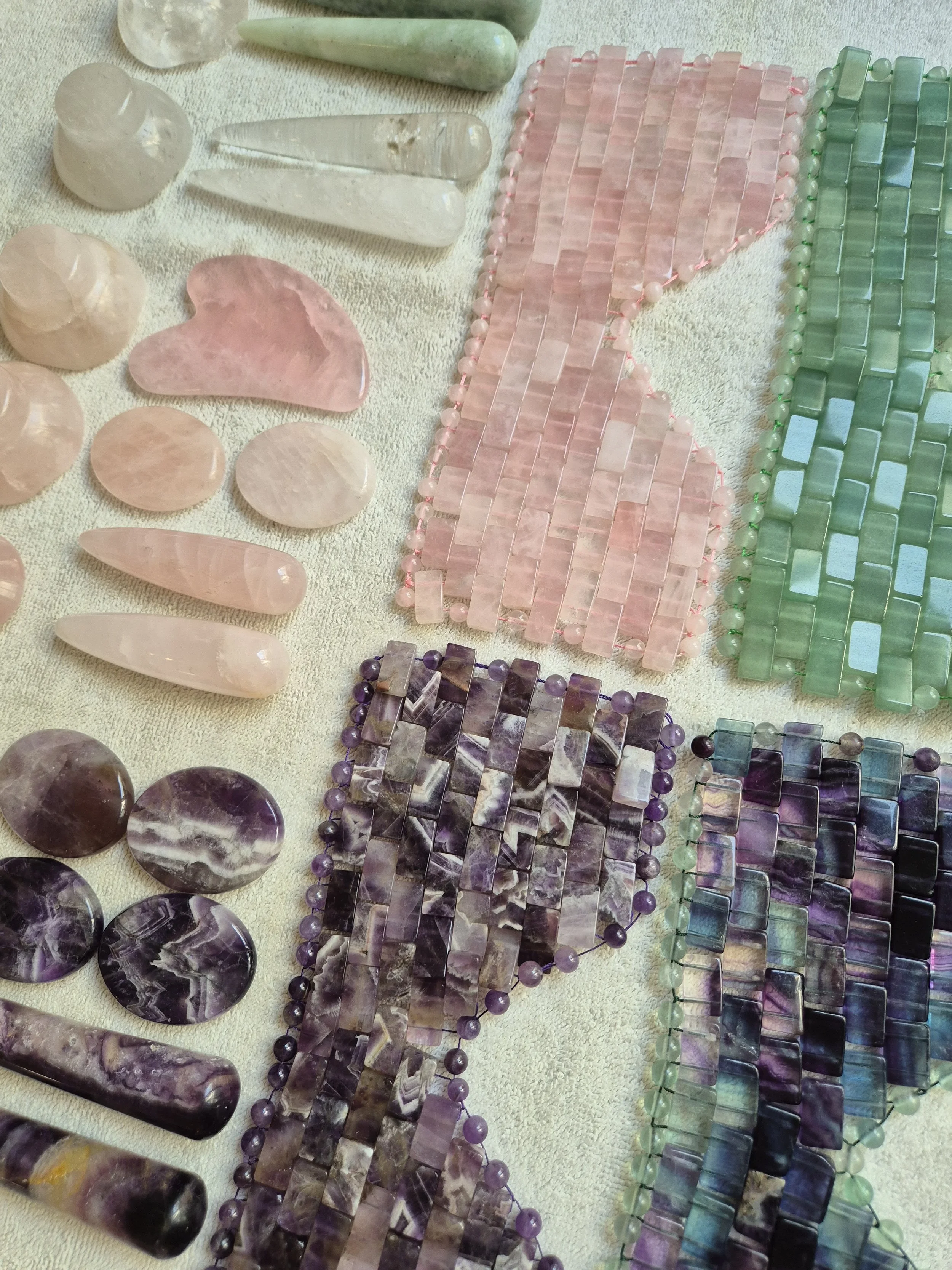 Various colorful semi-precious gemstone beads and shaped stones arranged on a cloth, including pink, green, purple, and black stones.