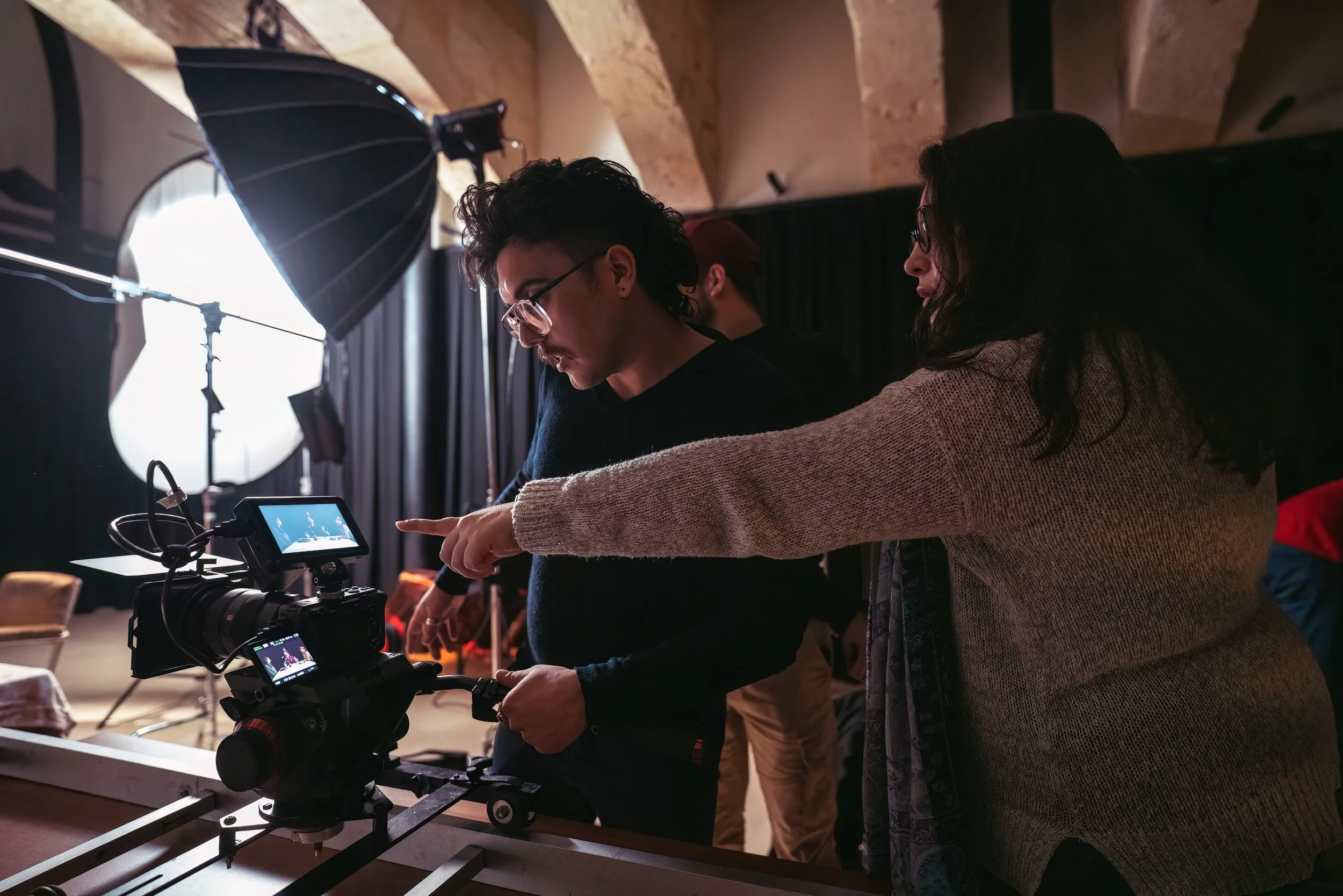 A man and woman behind a film camera discussing composition