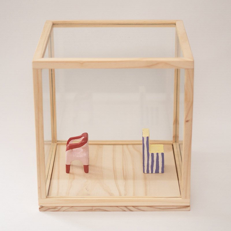 "Musical Chairs" is a series of miniature sculptures by Valentina Grisales that captures the essence of the everyday object transformed into visual poetry. Enclosed in wooden and glass showcases, these chairs take on different shapes and colors, unleashing a new