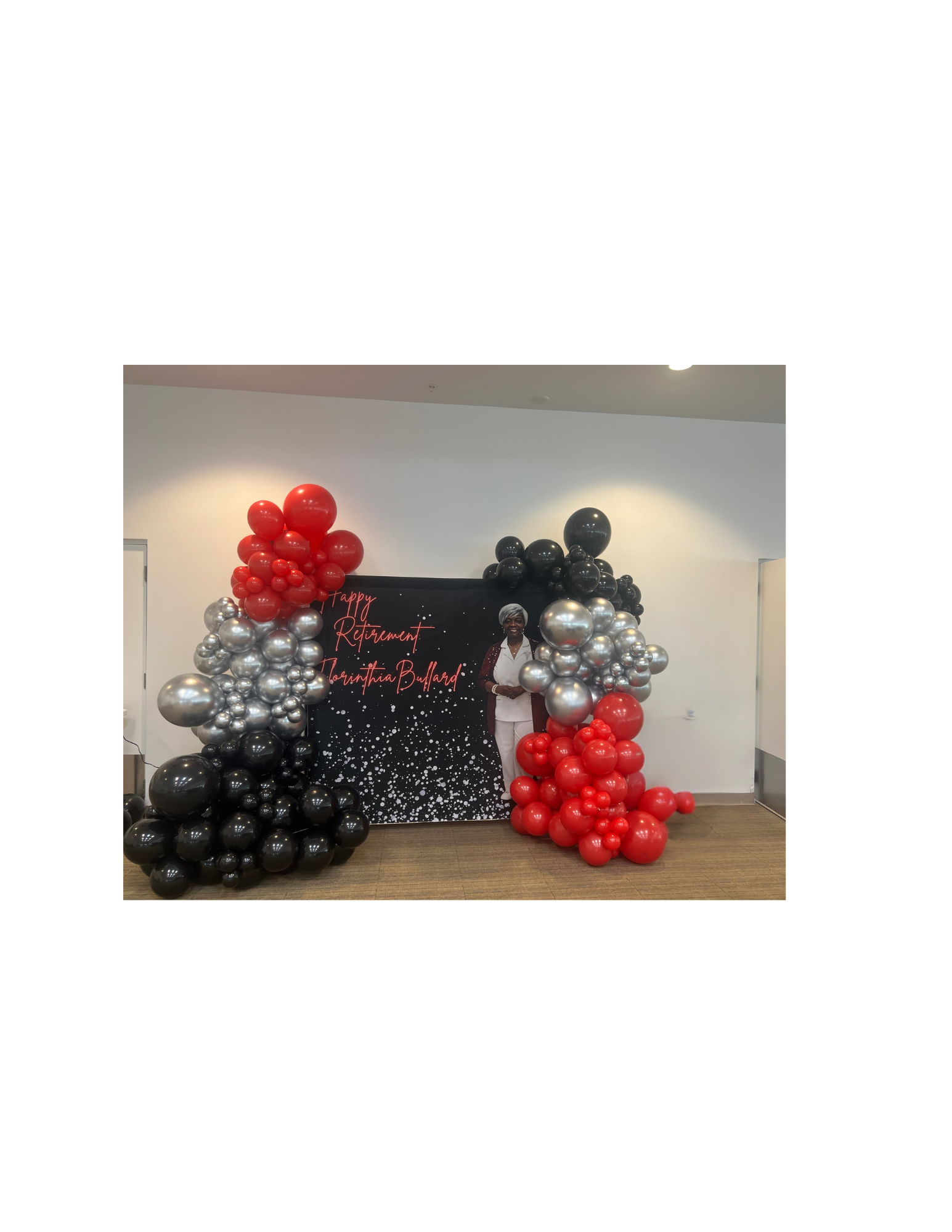 Balloon arch with red, black, and silver balloons surrounding a photo display and a sign that says "Happy Retirement, Tarrantina Bullard."