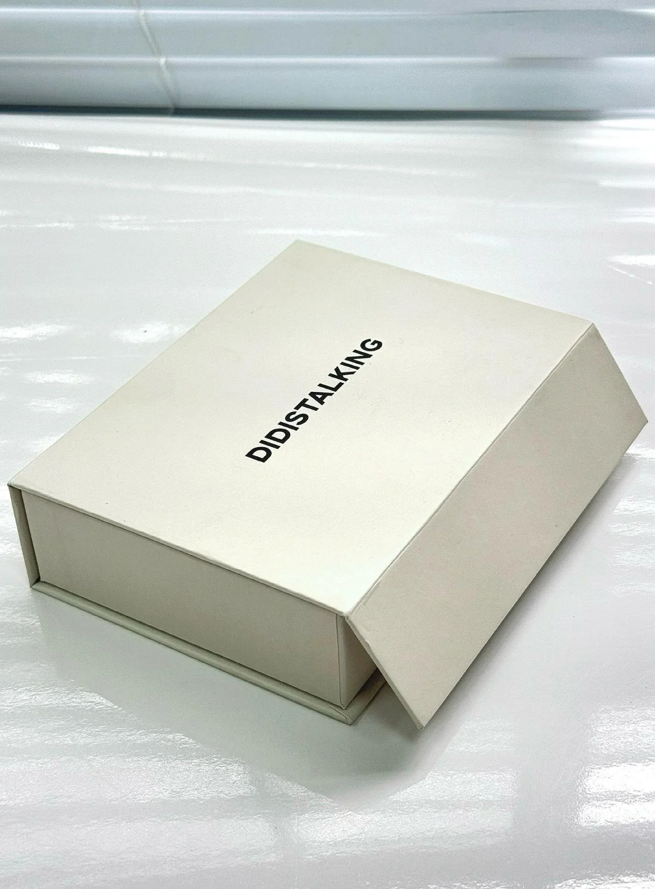 En vit låda med texten 'DIDISTALKING' på toppen, placerad på en vit yta.