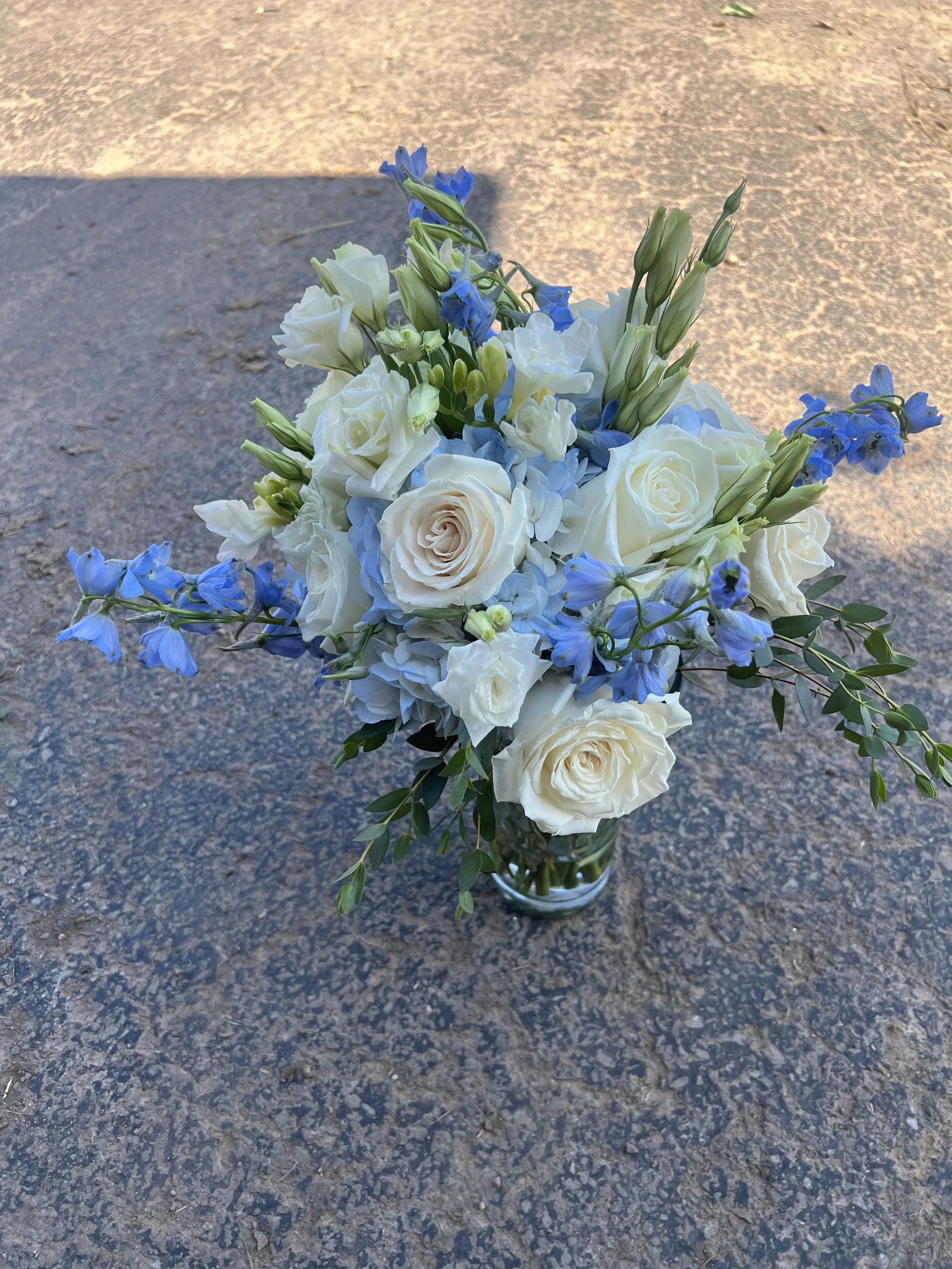 A bouquet of white and blue flowers in a glass vase on a textured outdoor surface.