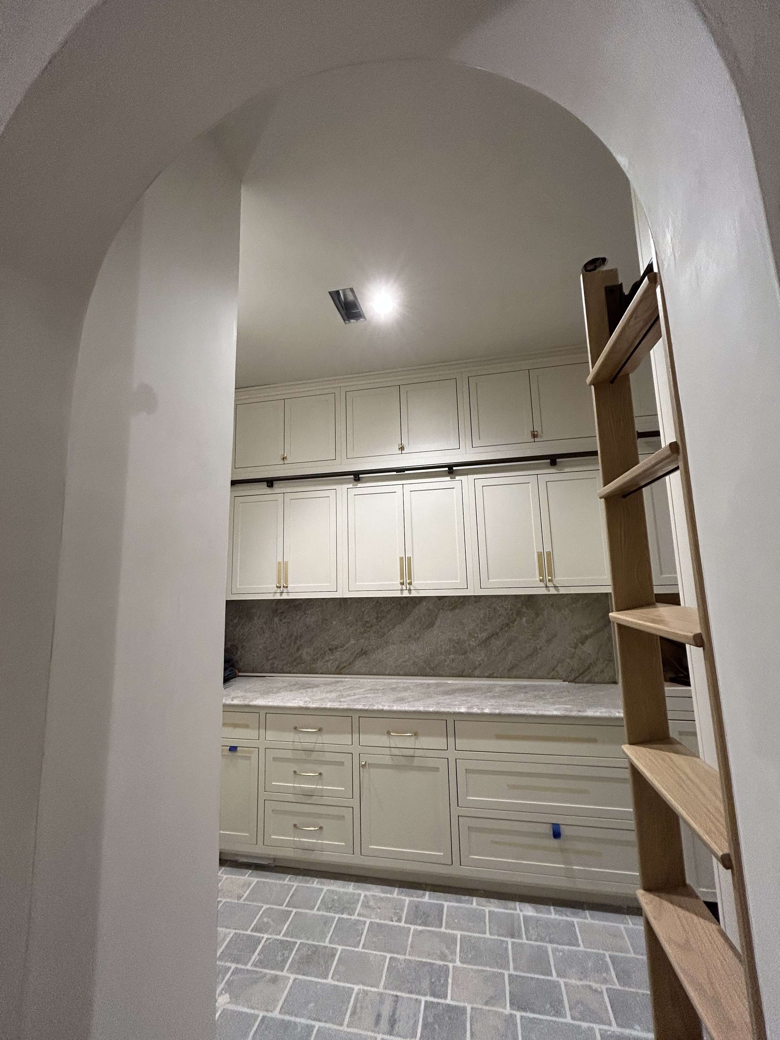 Kitchen with white cabinets, grey marble countertops, tile floor, and a ladder leaning against the wall.