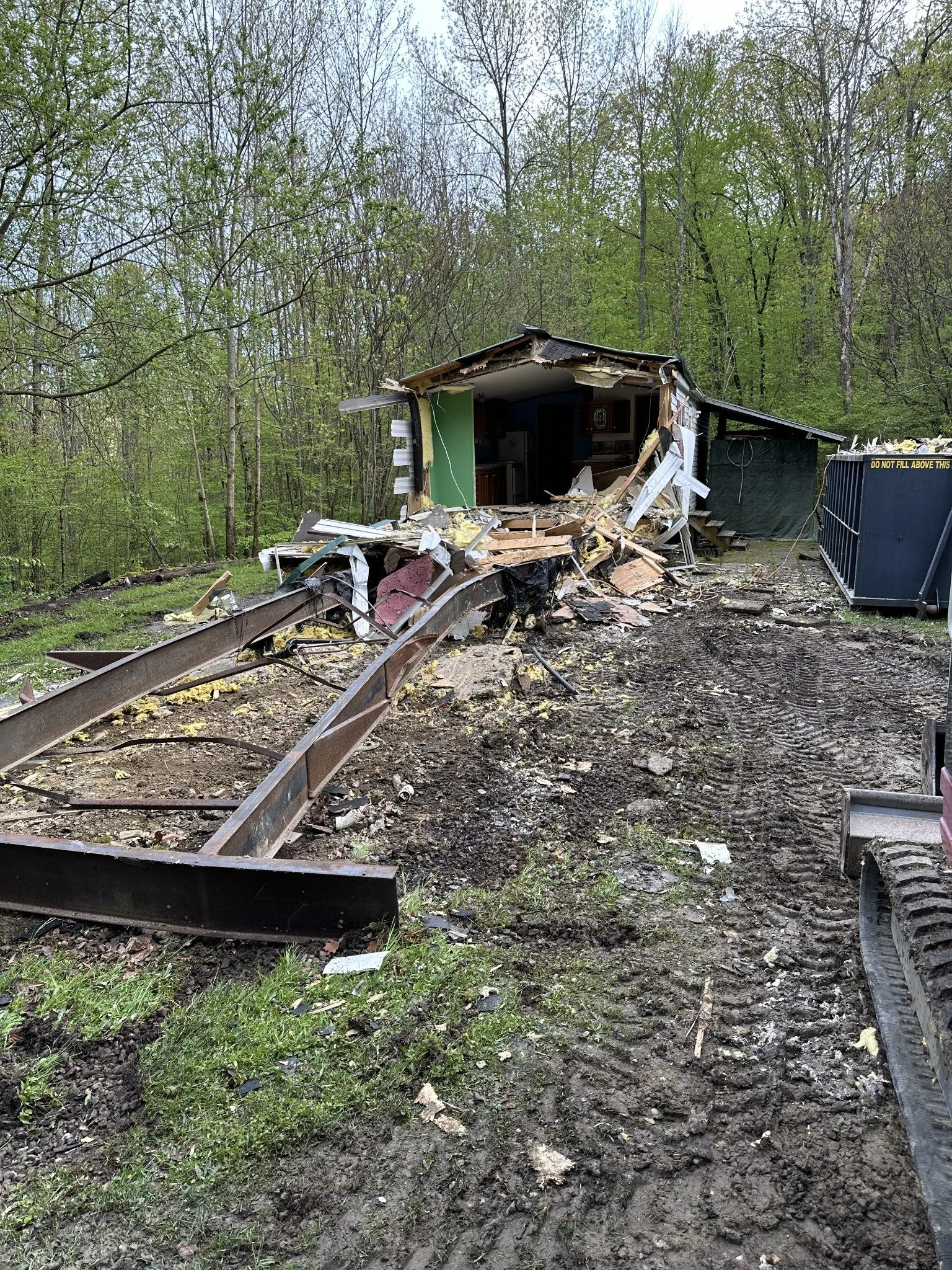 Partially destroyed small building in a wooded area with construction debris and a track on the ground.