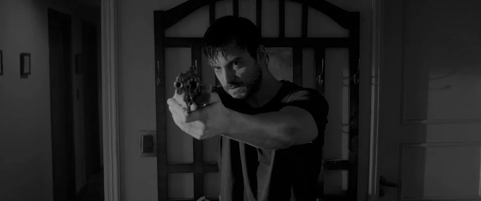 El holding a handgun, preparing to shoot open the apartment door.