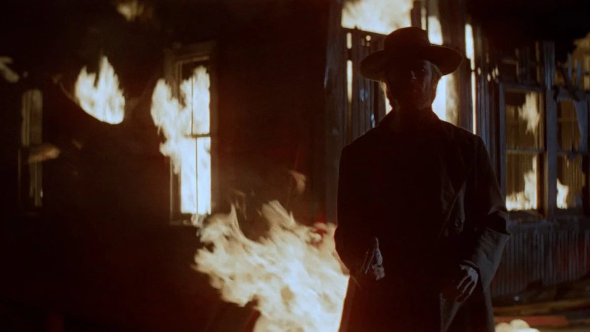 Clint Eastwood as "The Stranget" brandishes a gun while standing against a background of a burning building.