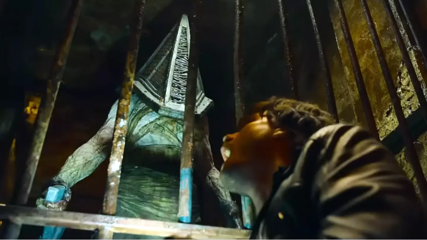 A still from Return To Silent Hill showing Pyramind Head standing behind metal bars. He looks like a computer rendered character.