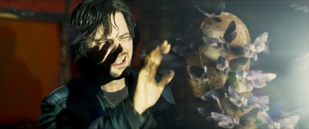 Jeremy Irvine as James Sunderland. There is light in his eyes and a manequin covered in moths in front of him, backlit from the right of the screen.