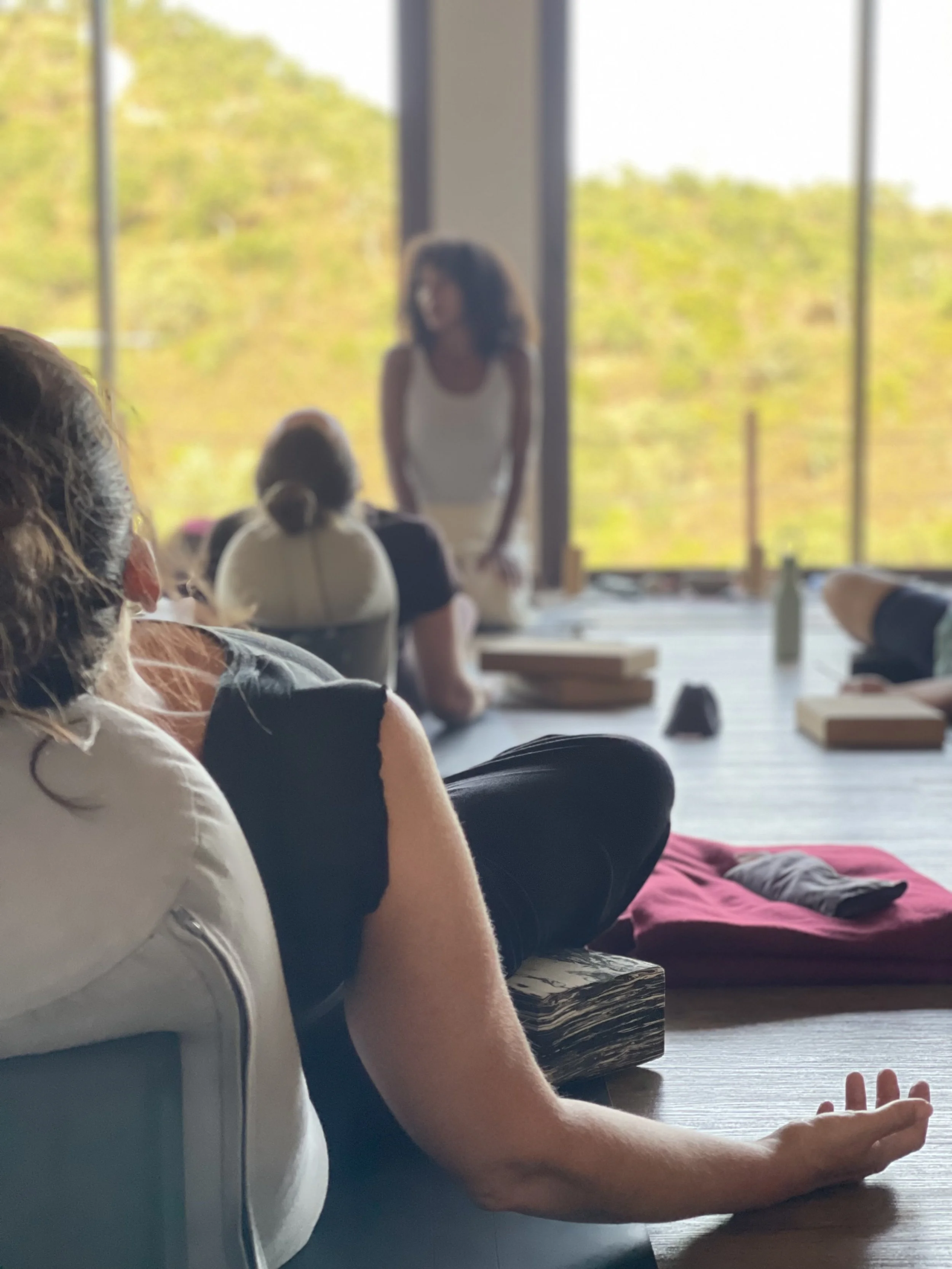 People participating in a yoga class or meditation session in a room with large windows overlooking a green, wooded landscape, on a yoga retreat in Portugal.