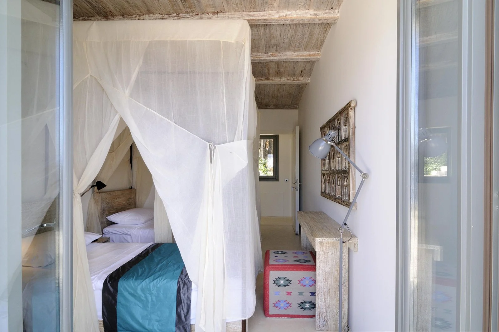 Bedroom with bed, pillows, sliding glass door to balcony with outdoor chairs, and minimalist furniture.