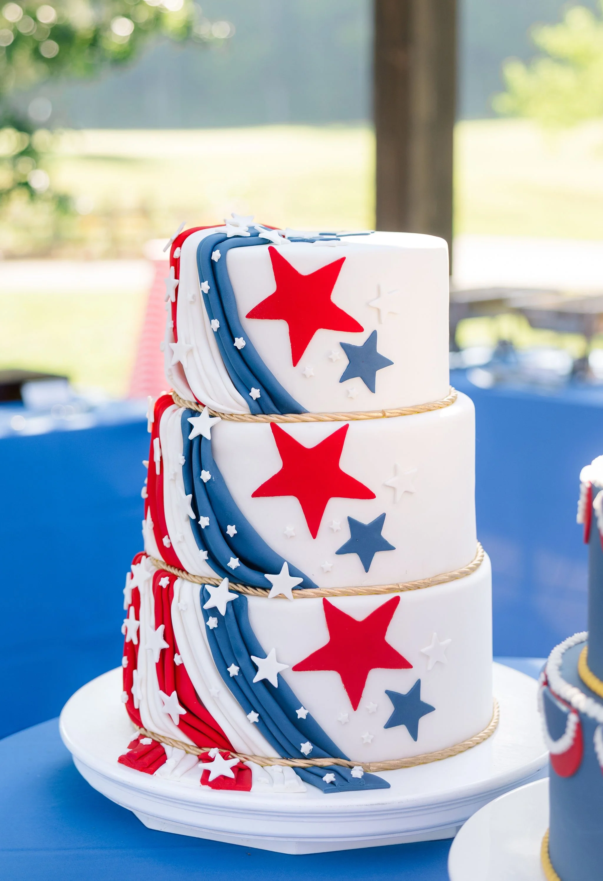 Patriotic tiered cake to celebrate America's 250th birthday. Red, white and blueFondant drapes down a white cake with stars and braided "rope"