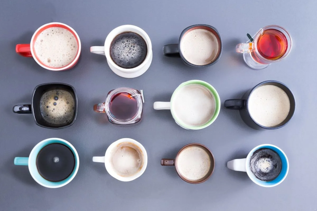 Multiple cups of coffee and tea are arranged in rows.