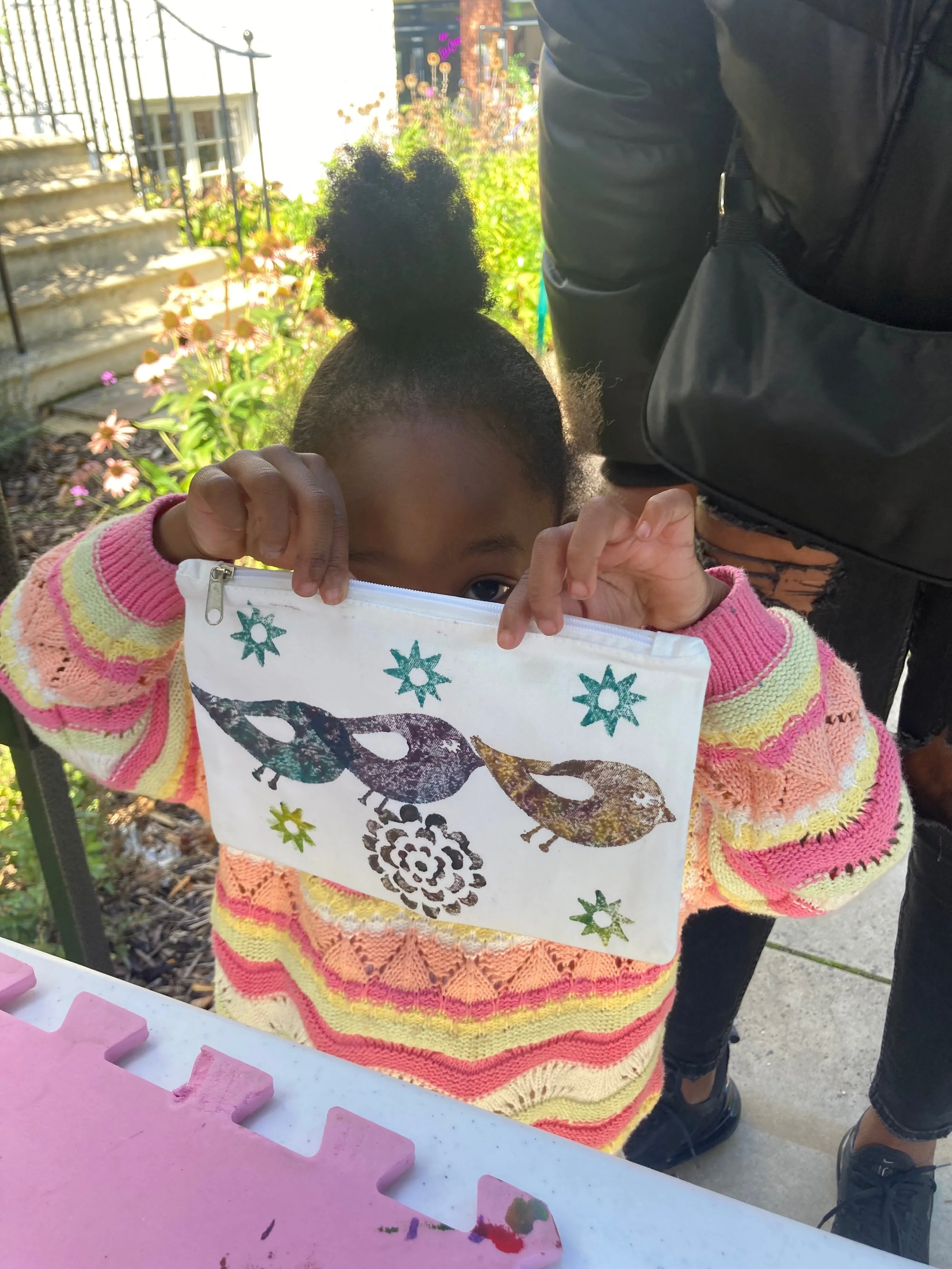 Image of a young workshop attendee holding up their block printed pencil case with three little birds printed on it