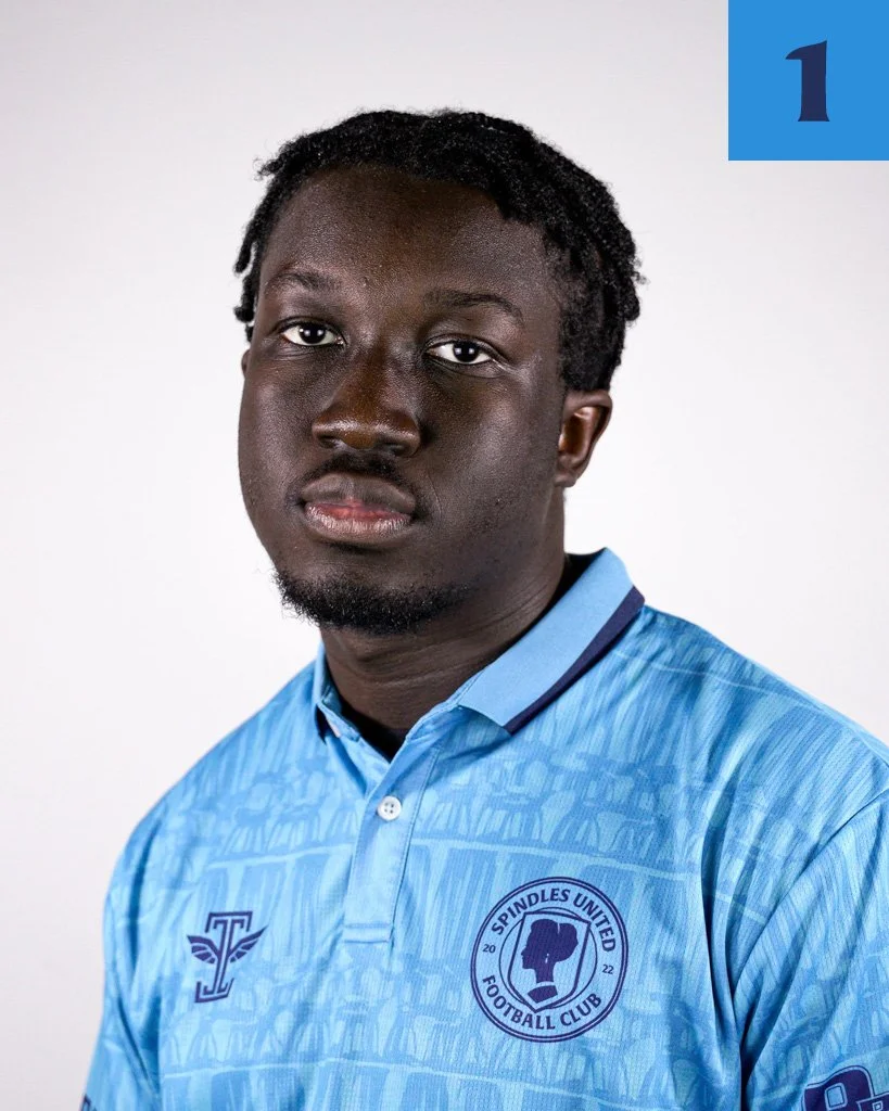 Portrait of a young black man in a blue sports jersey with the Spindles United Football Club logo, against a white background.