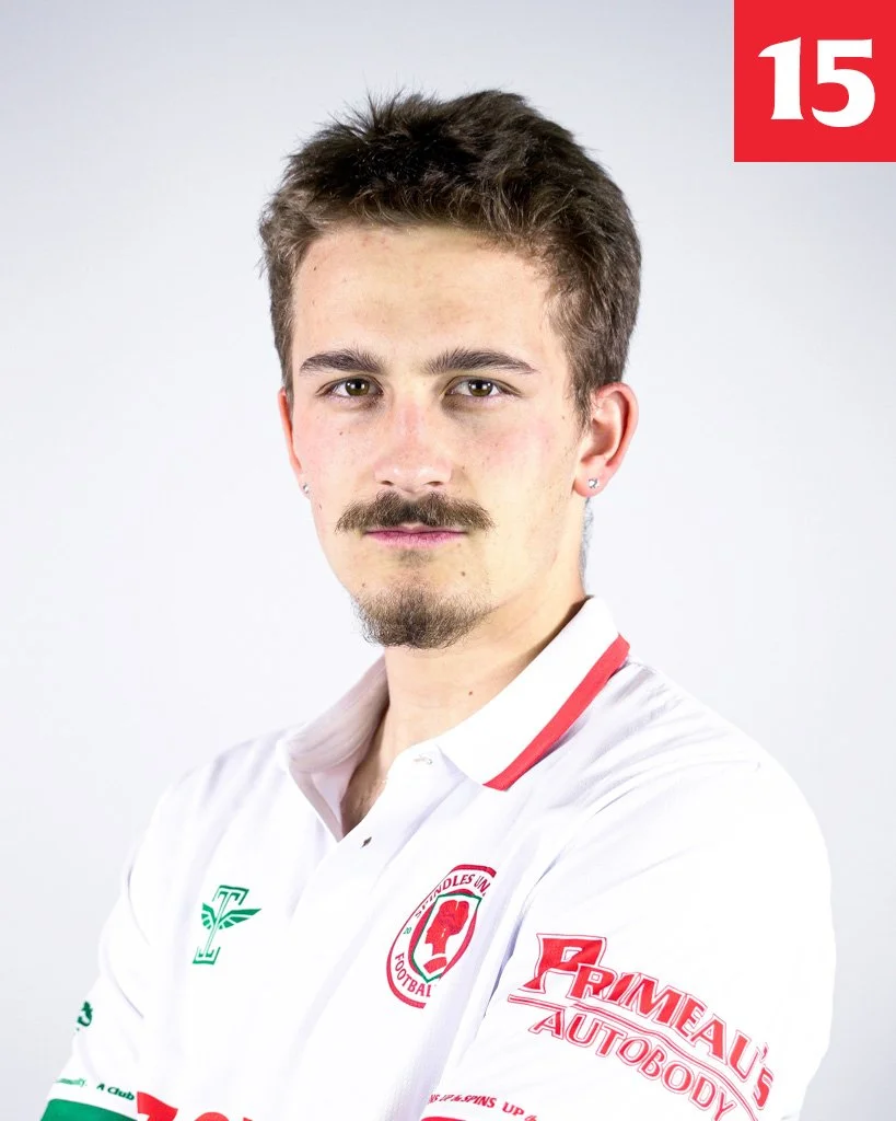 Portrait of a young man with brown hair, mustache, and goatee, wearing a white sports jersey with logos, against a plain light grey background.