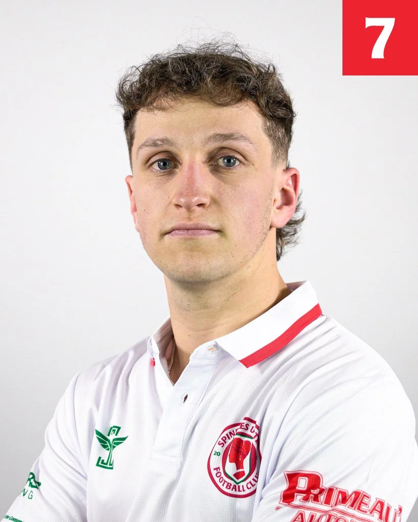 A portrait of a young man with curly brown hair, wearing a white sports jersey with red and green accents, featuring a football club emblem and logos.