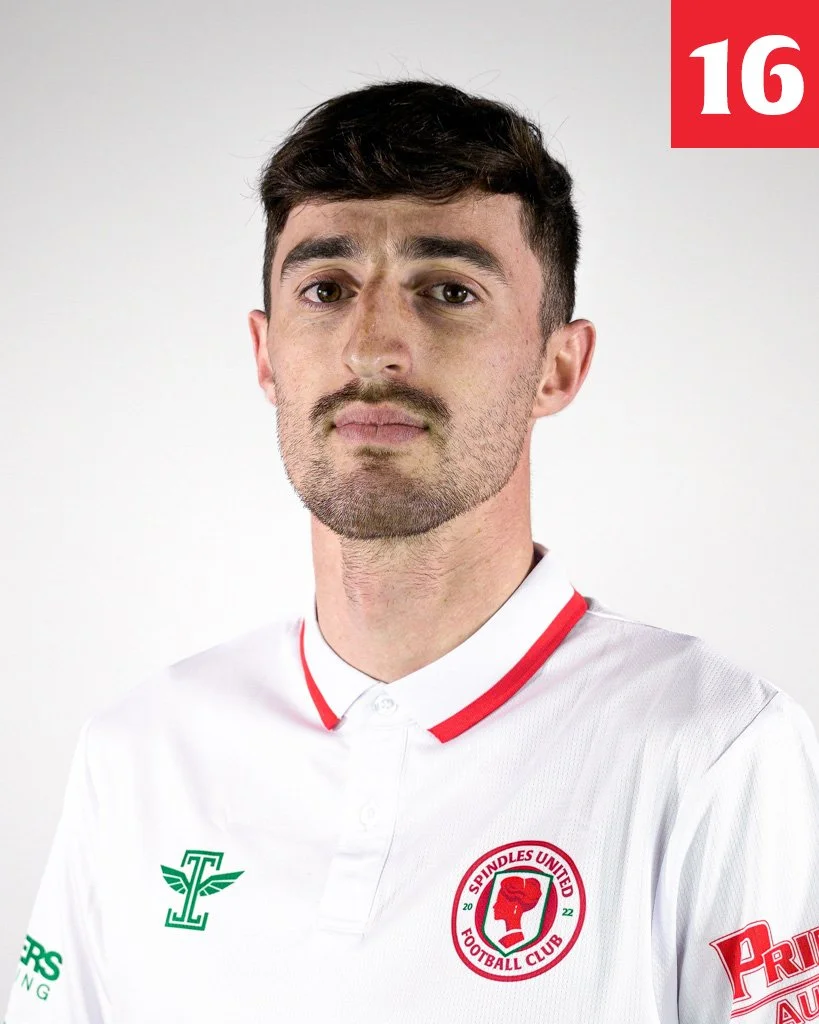 A man with dark brown hair, a short beard, and light skin wearing a white football jersey with red accents, the Spindles United Football Club logo, and various sponsor logos, standing against a plain white background.