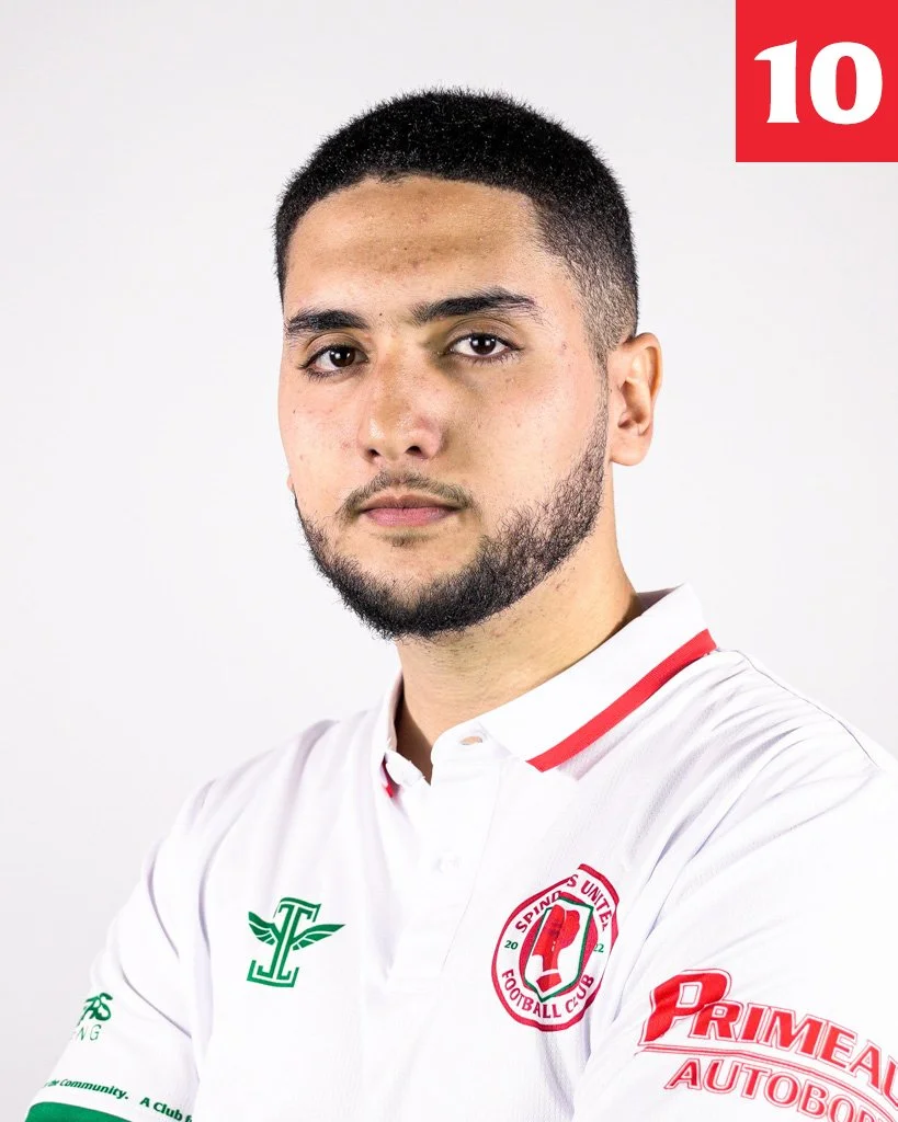 A young man with short dark hair and a beard wearing a white sports polo shirt with red and green accents, logo of Sporting United Football Club, and sponsor logos, standing against a plain white background.