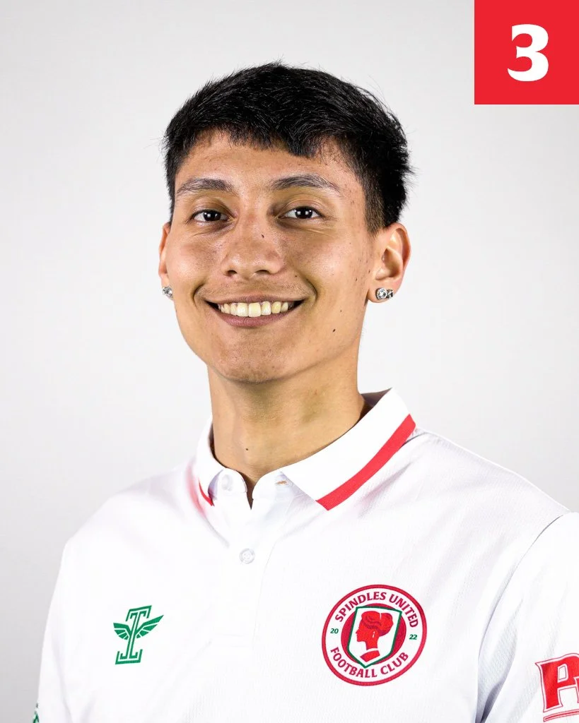 A smiling young man with short dark hair and earrings, wearing a white sports polo shirt with red accents and the Spindles United Football Club logo, standing against a plain white background.