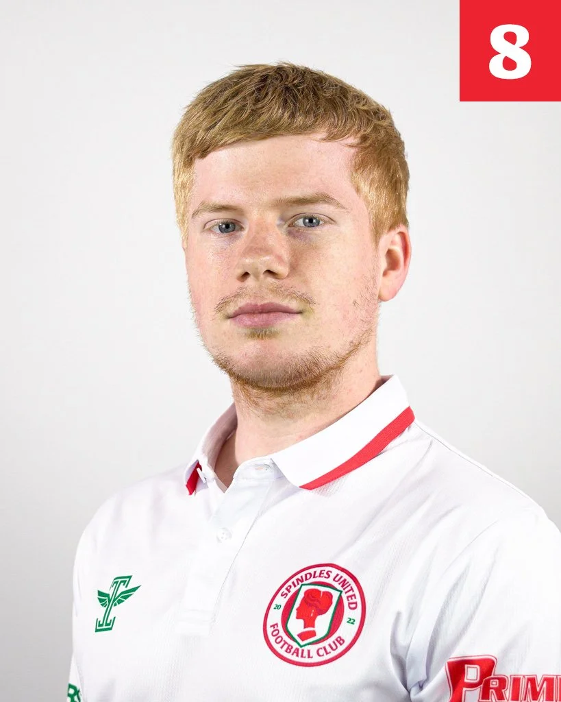 A young man with light skin, red hair, and a light beard wearing a white sports jersey with red accents and the Spindles United Football Club logo.