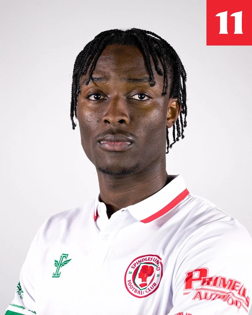 Portrait of a young man with braided hair wearing a white football jersey with red and green accents, featuring the Spindles Union Football Club logo on the chest and various sponsor patches on the sleeves.